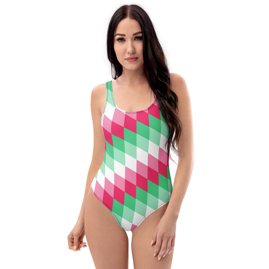 A woman or non binary person with long dark hair is wearing a one-piece swimsuit with a diamond pattern angled top left to bottom right. The interlocking diamonds are in layered colours, and the layers are made from the colours of the Abrosexual Pride Flag 