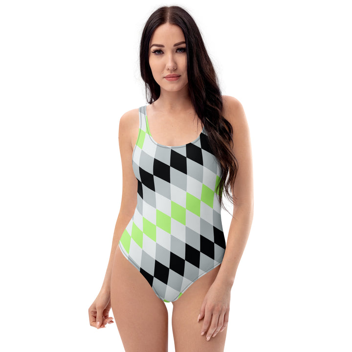 A woman or non binary person with long dark hair is wearing a one-piece swimsuit with a diamond pattern angled top left to bottom right. The interlocking diamonds are in layered colours, and the layers are made from the colours of the Agender Pride Flag 
