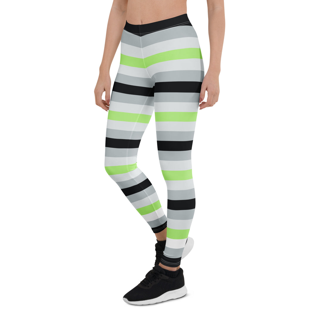 A person wears a pair of leggings with the repeated colours of the Agender pride flag all down them, and black trainers. 