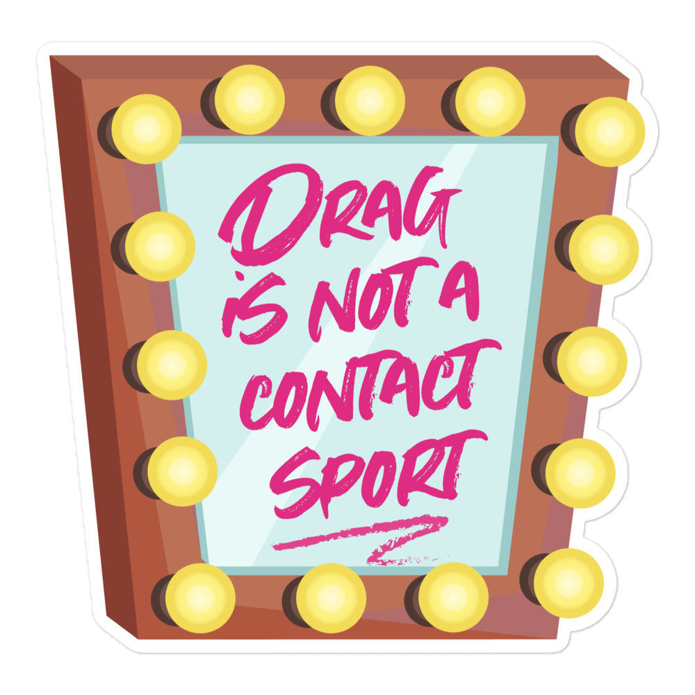 The sticker shows a cartoon illustration of a make up mirror, with a brown frame and 16 yellow lights around it. On the mirror in pink lipstick is written Drag Is Not A Contact Sport, with an underlined flourish. 