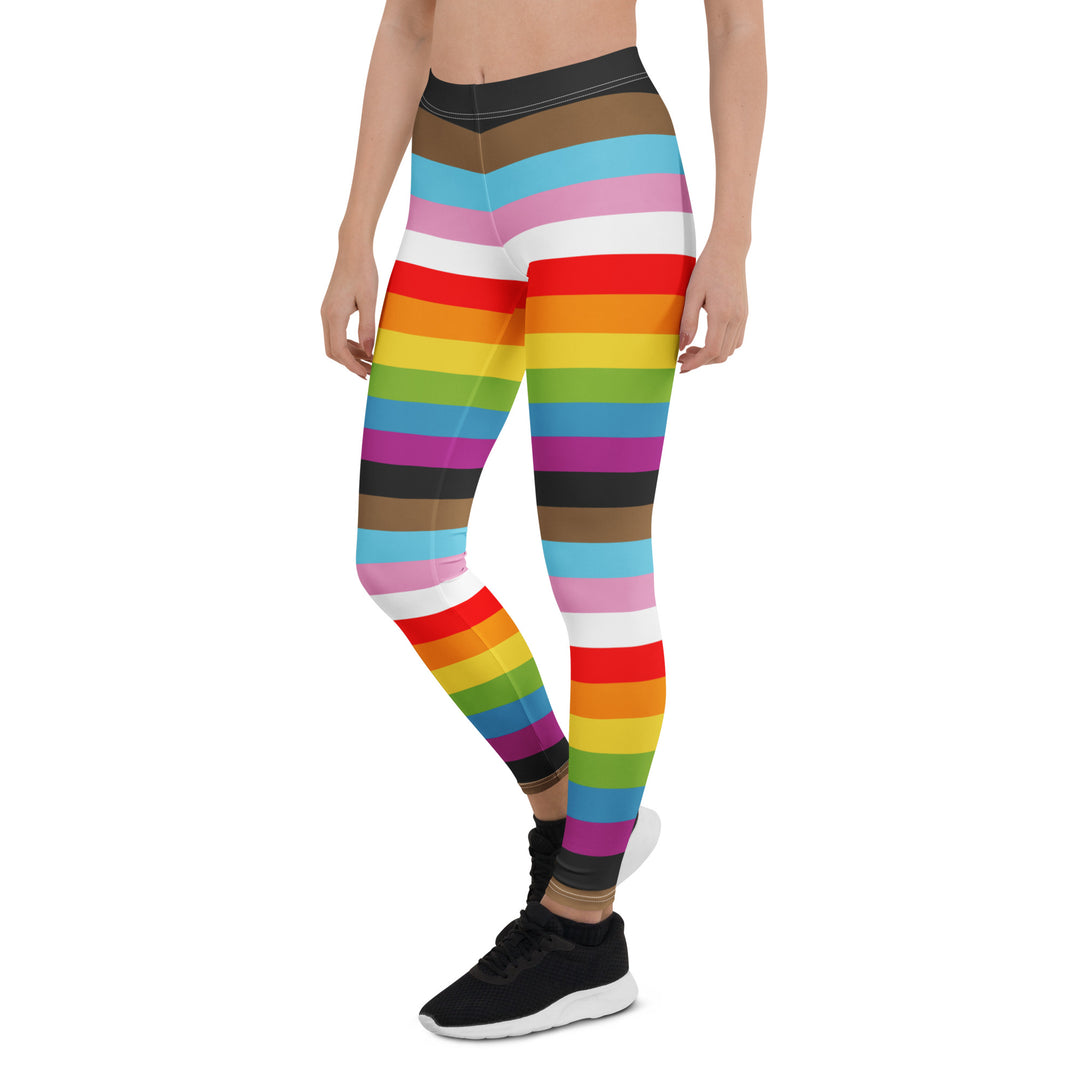 A person wears a pair of leggings with the repeated stripes of the Progress Pride Flag down them, and black trainers. 
