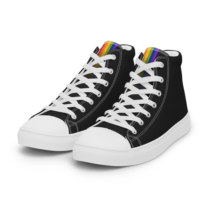 A pair of black high top trainers on a white background with a Rainbow Pride Flag at the top of the tongue that fade out under the laces. By The Rainbow Stores